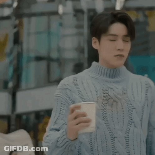 A Man In A Blue Sweater Is Holding A Cup Of Coffee In A Restaurant . GIF