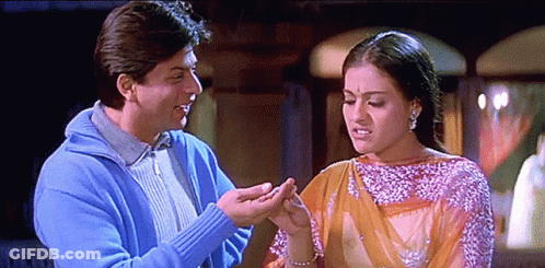 A Man In A Blue Sweater Is Holding A Woman 'S Hand In Front Of Her Face GIF