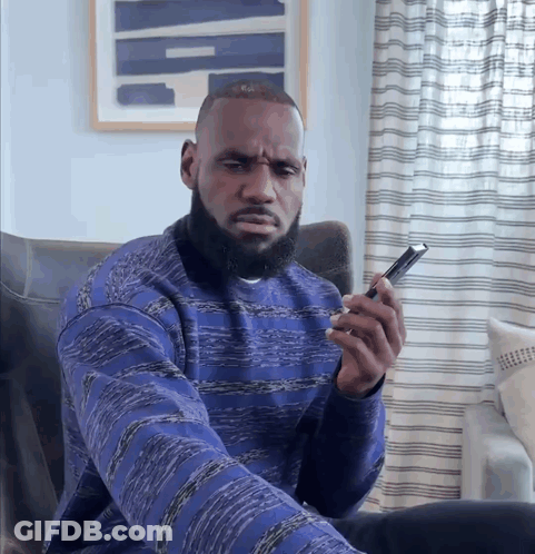 A Man In A Blue Sweater Is Looking At His Phone GIF