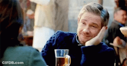 A Man In A Blue Sweater Is Sitting At A Table With A Glass Of Beer In Front Of Him . GIF