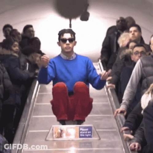 A Man In A Blue Sweater Is Sitting On An Escalator GIF