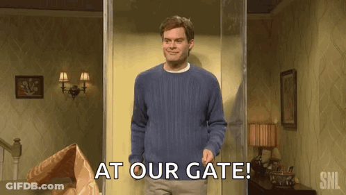 A Man In A Blue Sweater Is Standing In A Doorway With The Words `` At Our Gate '' Written On It . GIF