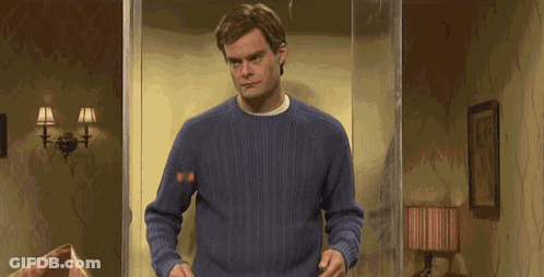 A Man In A Blue Sweater Is Standing In A Living Room With A Lamp . GIF