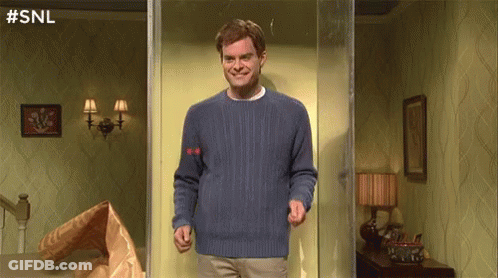 A Man In A Blue Sweater Is Standing In A Room With A Bag Of Food . GIF