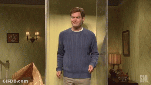 A Man In A Blue Sweater Is Standing In A Room With The Letters Snl On The Wall GIF