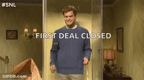 A Man In A Blue Sweater Is Standing In A Room With The Words `` First Deal Closed '' Written On The Screen . GIF