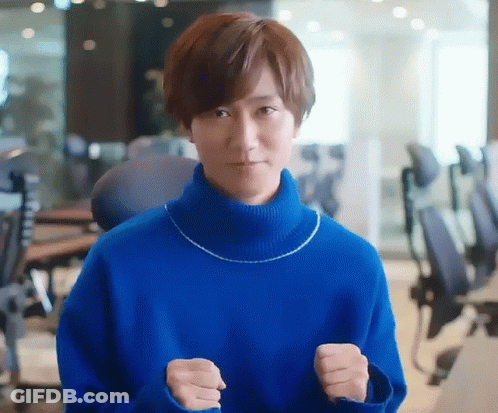 A Man In A Blue Sweater Is Standing In An Office With His Fists Up . GIF