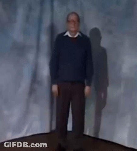 A Man In A Blue Sweater Is Standing In Front Of A Blue Curtain . GIF