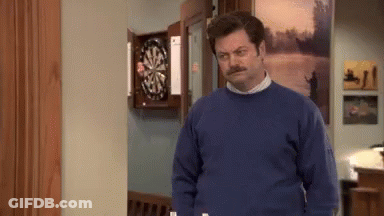 A Man In A Blue Sweater Is Standing In Front Of A Dartboard GIF
