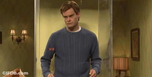 A Man In A Blue Sweater Is Standing In Front Of A Glass Door In A Room . GIF