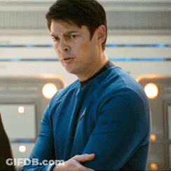 A Man In A Blue Sweater Is Standing In Front Of A Laptop Computer . GIF