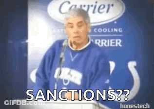 A Man In A Blue Sweater Is Standing In Front Of A Podium With The Words Sanctions On It . GIF