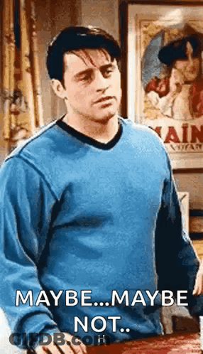 A Man In A Blue Sweater Is Standing In Front Of A Table And A Poster . GIF