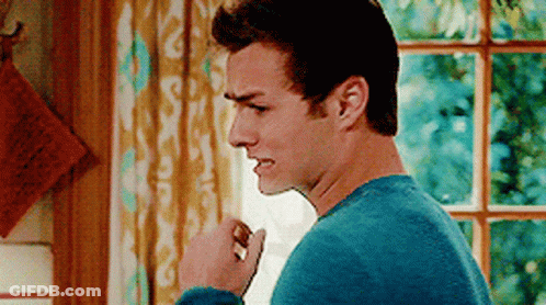 A Man In A Blue Sweater Is Standing In Front Of A Window With His Fist In The Air . GIF