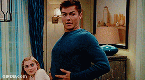 A Man In A Blue Sweater Is Standing Next To A Woman In A White Sweater . GIF