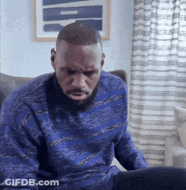 A Man In A Blue Sweater Sits In Front Of A Laptop Computer GIF
