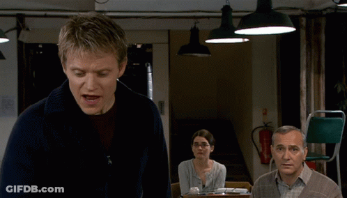 A Man In A Blue Sweater Stands In Front Of A Fire Extinguisher GIF