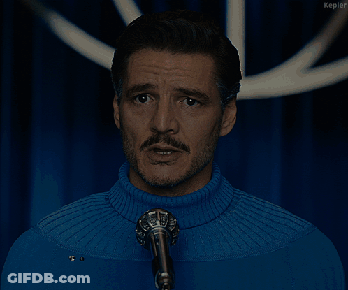 A Man In A Blue Sweater Stands In Front Of A Microphone With The Words We Will Protect You Below Him GIF