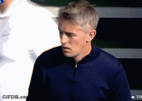 A Man In A Blue Sweater Stands In Front Of A Tov Sign GIF