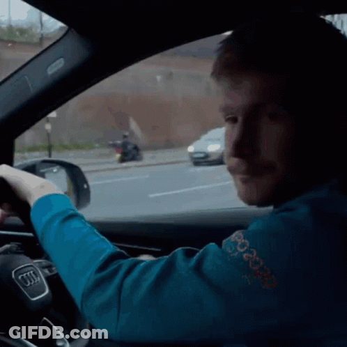 A Man In A Blue Sweater With The Word Peace On It Is Driving An Audi GIF