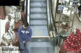 A Man In A Blue Sweatshirt Is Standing On An Escalator . GIF