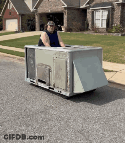A Man In A Blue Tank Top Is Driving A Small Vehicle On The Street GIF