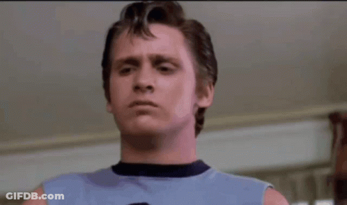 A Man In A Blue Tank Top Is Holding A Pair Of Scissors In His Hand . GIF