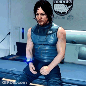 A Man In A Blue Tank Top Is Sitting In Front Of A Wall That Says Bridges GIF