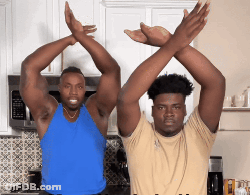 A Man In A Blue Tank Top Stands Next To A Man In A Tan Shirt GIF