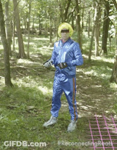 A Man In A Blue Tracksuit Is Standing In The Woods With The Hashtag #Reconnectingroots GIF