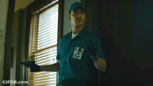 A Man In A Blue Uniform Holds A Gun In Front Of A Window With Blinds .. GIF