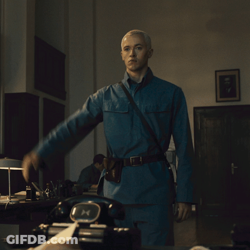 A Man In A Blue Uniform Is Standing In Front Of A Black Telephone GIF