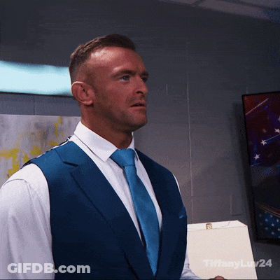 A Man In A Blue Vest And Tie Is Standing In Front Of A Wall With Tiffanylaw24 Written On It GIF