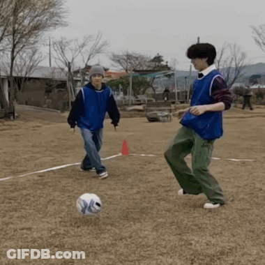 A Man In A Blue Vest Is Kicking A Soccer Ball While Another Man Watches GIF