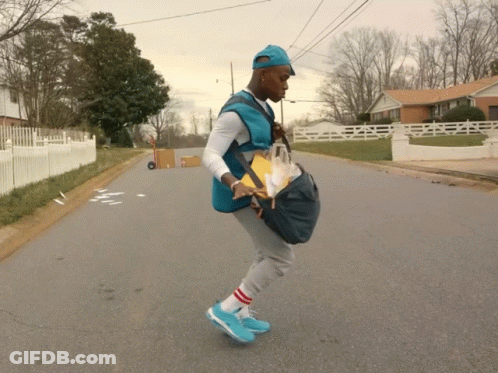 A Man In A Blue Vest Is Walking Down A Street With A Bag On His Back GIF