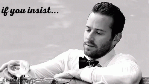 A Man In A Bow Tie Is Sitting At A Table With A Glass Of Wine In His Hand . GIF