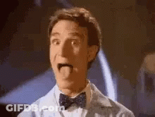 A Man In A Bow Tie Is Sticking His Tongue Out And Making A Funny Face . GIF