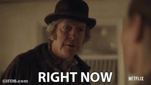 A Man In A Bowler Hat Is Talking To Another Man And Says Right Now . GIF