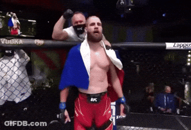 A Man In A Boxing Ring With A Flag Draped Over His Shoulder GIF