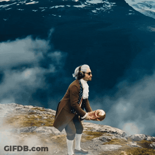 A Man In A Brown Coat And White Polka Dot Scarf Stands On A Rocky Hill GIF