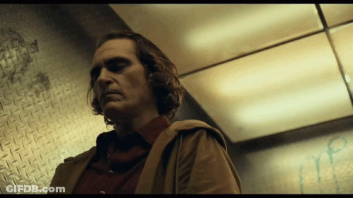 A Man In A Brown Coat Stands In A Dark Room GIF