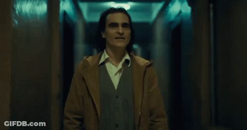 A Man In A Brown Coat Stands In A Hallway GIF