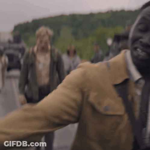 A Man In A Brown Jacket And Tie Is Standing In Front Of A Crowd . GIF