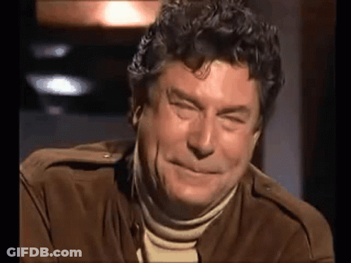 A Man In A Brown Jacket And Turtleneck Is Laughing . GIF