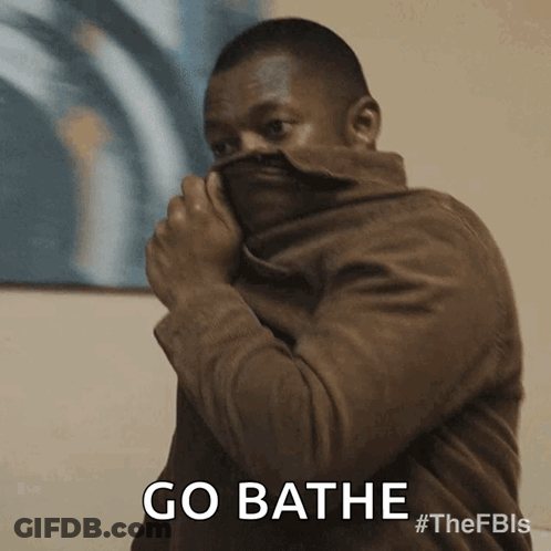 A Man In A Brown Jacket Is Covering His Face With His Jacket And Says Go Bathe GIF