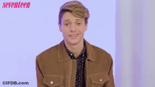 A Man In A Brown Jacket Is Smiling In Front Of A Seventeen Ad GIF