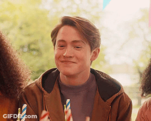 A Man In A Brown Jacket Is Smiling While Holding A Straw GIF