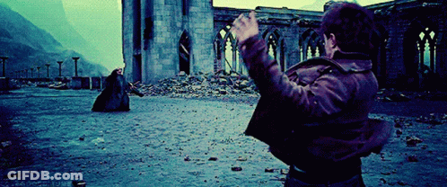 A Man In A Brown Jacket Is Standing In Front Of A Ruined Building With His Hands In The Air GIF