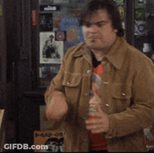 A Man In A Brown Jacket Is Standing In Front Of A Wall With Stickers On It Including One That Says ' Nike ' GIF