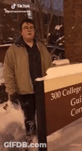 A Man In A Brown Jacket Is Standing Next To A Sign That Says `` 300 College Gui 'S Court '' . GIF